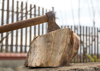 An old ax with a long handle sticks out of the stump. Sunny summer day. Ax for cutting firewood. An old ax was stuck in a stump on the farm