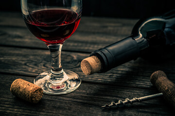 Bottle of red wine with a glass and corkscrew with cork on an old wooden table. Angle view