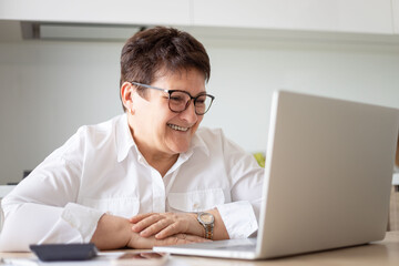 Smiling mature middle aged business woman using laptop working on computer,distance learning from home office, conference calling in virtual chat meeting.