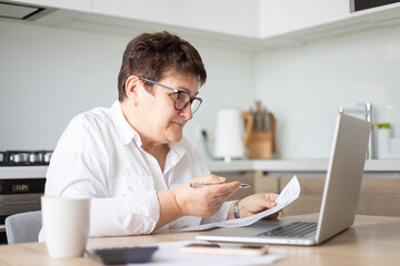 mature middle aged business woman using laptop working on computer with documents, sitting at desk. 