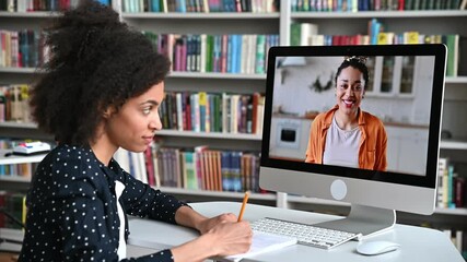 Wall Mural - Side view of an African American clever female student during online lecture. African American female tutor conducts online lesson, female student takes notes. Online training, video call