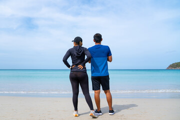 Wall Mural - Happy confidence Asian family man and woman enjoy outdoor lifestyle activity beach running at tropical beach in summer vacation. Healthy couple in sportswear jogging together in summer sunny day.