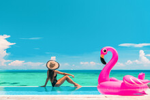 Vacation Summer Fun Woman Sunbathing With Inflatable Pink Flamingo Pool Float By Infinity Swimming Pool. Luxury Travel Holiday At Overwater Villa Resort.