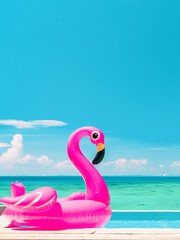 Summer vacation fun vertical crop of pink flamingo swimming pool toy float floating on infinity luxury resort pool with blue ocean background.