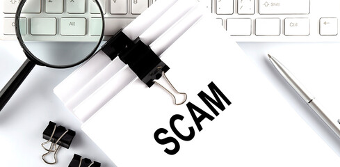 Poster - text scam on paper on the keyboard with office tools