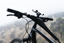 Black Bicycle Handlebars With Cellphone Holder And Mountains On Blurred Background On Foggy Day. Sport Adventure Concept