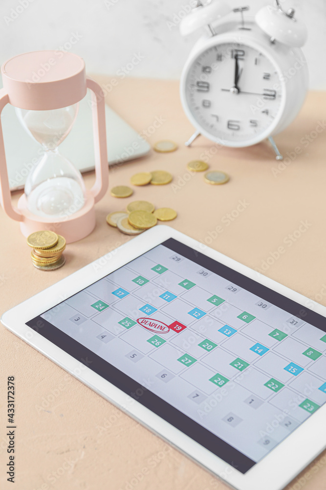 Tablet computer with hourglass on color background. Deadline concept