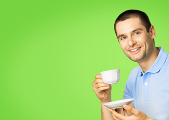 Portrait of young happy smiling man in blue casual clothing drinking coffee, isolated over green color background.