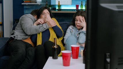 Group of mixed race person relaxing comfortable on couch while watching horror film during movie evening. Multi-racial friends having scary reaction spending time together late at night