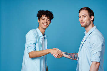 curly guy in a shirt stands next to a young man in a t-shirt on a blue background cropped view