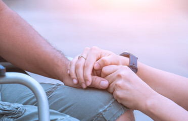 Close up image of woman hands holding her husband's hand on wheelchair during rehabilitation for encouragement in outdoor area