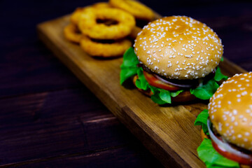 Closeup top view shot of two delicious tasty yummy hamburgers bun with beef tomato and lettuce serve with fried onion rings on wood plate decorated on sack cloth with parsley on dark old wooden table