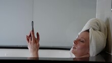 European Woman Using Mobile Phone Taking Bath In Bathroom