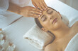 © rogerphoto - Beautiful brunette woman enjoying facial massage with closed eyes in sunny spa center. Relaxing treatment and cosmetic medicine concepts