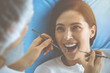© rogerphoto - Smiling brunette woman being examined by dentist at dental clinic. Hands of a doctor holding dental instruments near patient's mouth. Healthy teeth and medicine concept