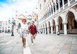 © Davide Angelini - Couple of tourists visiting Venice, Italy - Boyfriend and girlfriend in love running together on city street at sunset - People, love and holidays concept