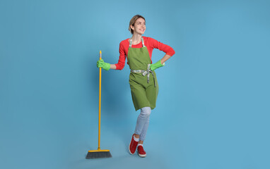 Poster - Young housewife with broom on light blue background