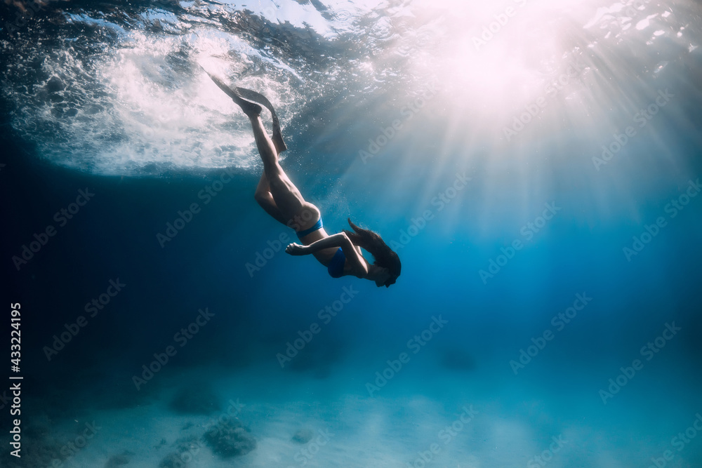 Attractive free diver woman with fins dive at deep underwater in sea. - obrazy, fototapety, plakaty 