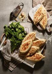 Wall Mural - Oriental cuisine. Tortillas with cheese and herbs. Fried dough with a filling of suluguni and coriander, with garlic and salt on a light gray background. Rustic. Flatlay, top view. Background image