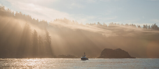 Atmospheric golden light sunbeams through morning mist and fog over an ocean fishing boat off the pacific coast of Vancouver Island near Port Renfrew, BC, Canada.