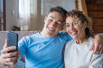 Wall Mural - Smiling middle-aged 40s mother rest with grown-up son using smartphone together, happy young man enjoy family weekend with mom browsing wireless Internet on cellphone, have fun at home
