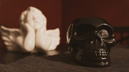 Poster - Selective focus shot of a black skull sculpture with a blurred white angel background