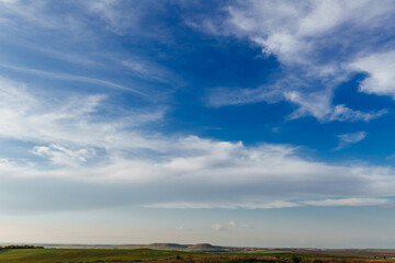 Wall Mural - white clouds stretched across the blue sky on a warm sunny day, and under the sky were green fields 