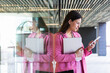 © NOVELLIMAGE/Westend61 - Female young entrepreneur with laptop using mobile phone while leaning on glass wall
