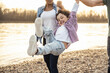 © Uwe Umst√§tter/Westend61 - Cheerful boy holding hands of parents while swinging by lake