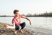 Cheerful Young Man Throwing Pebble In Lake On Sunny Day