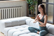 © BestForYou - Relaxed woman meditates with closed eyes in a prayer position on the sofa at home.