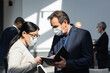 © LIGHTFIELD STUDIOS - mature businessman in medical mask showing notebook to asian colleague