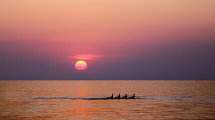 People silhouettes on rowing boat in front of sunset background. Front view