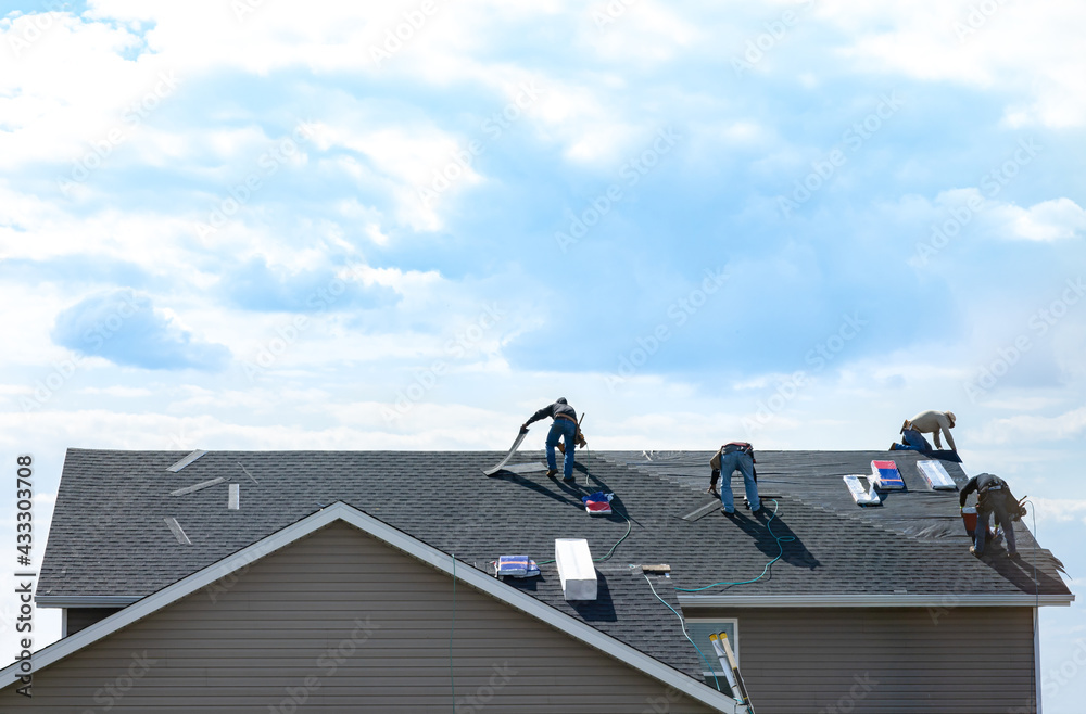 4 construction workers fixing roof against clouds blue sky, install shingles at the top of the house. Renovate, improvement, build home exterior by professional teamwork. Safety and protection concept - obrazy, fototapety, plakaty 