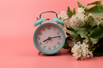 Blue vintage alarm clock with white lilac flowers, isolated on pink background, top view. Perfect morning concept. Deadline and change time concept.