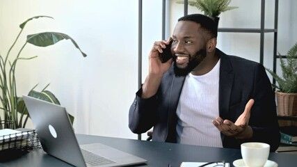 Wall Mural - Satisfied successful African American man, executive or top manager, sits at a workplace with, has a pleasant phone conversation with a friend or colleague. Phone talk using wireless smart phone