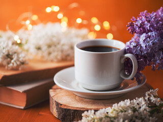 Wall Mural - A white cup of coffee on a wooden table. Blooming branches of white lilac, old books