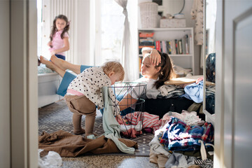 tired mother with small toddler daughter in messy bedroom at home, resting.