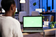 © DC Studio - Dark skin freelancer doing overwork in office with green screen latop sitting at desk in business office late at night. Businesswoman watching desktop with green mockup, chroma key, working overtime.