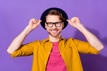 Wall Mural - Photo of charming young attractive man hold hands hat smile hipster isolated on purple color background