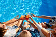 © artiemedvedev - Top view of of friends clinking glasses with fresh colorful cocktails sitting by swimming pool on sunny summer day. People toast drinking beverages at luxury villa poolside party on tropical vacation.