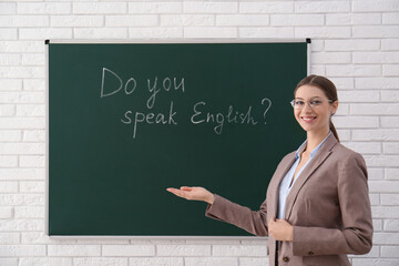 Canvas Print - Teacher near green chalkboard with inscription Do You Speak English? in classroom