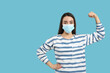 Woman with protective mask showing muscles on light blue background, space for text. Strong immunity concept