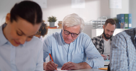 Diverse adult students in classroom with papers studying at courses