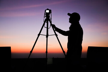 Poster - Silhouette of the photographer with tripod. Young Indian man taking photo with his camera during golden hour.