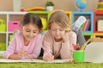 Wall Mural - Two cute little girls drawing with pencils while lying on floor