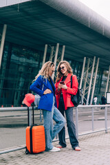 Two happy girls using smartphone checking flight or online check-in at airport together, with luggage. Air travel, summer holiday