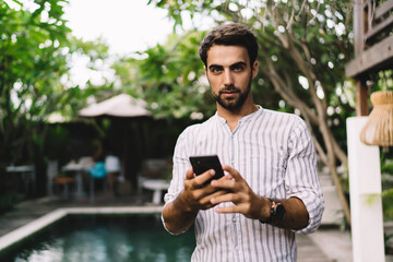 Wall Mural - Handsome young male blogger using smartphone on terrace