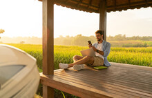 Positive Young Guy Chilling In Field Gazebo With Smartphone And Laptop
