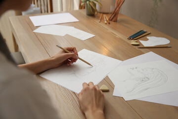 Young woman drawing male portrait at table indoors, closeup